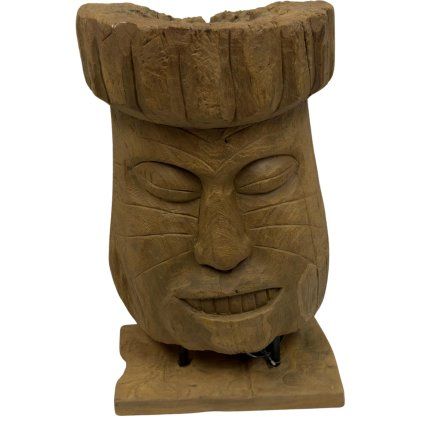 Tiki totem v podobě hlavy, precizně vyřezaný z teakového dřeva, umístěný na podstavci.