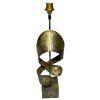 Indická kovová lampa s jemnými zlatavými odlesky a zdobením připomínajícím elegantně vinuté kovové pásy.