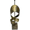 Indická kovová lampa s jemnými zlatavými odlesky a zdobením připomínajícím elegantně vinuté kovové pásy.