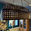 Velká závěsná lampa tvořená mosaznými kovovými proužky v proplétaném designu, voskovaná pro elegantní vzhled, ideální pro umístění nad stůl.